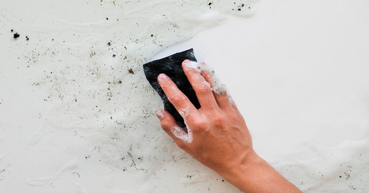 Mão a limpar ou raspar a parede afetada por bolor ou fungos. Dicas simples e eficazes para remover o bolor e proteger a saúde da sua família.